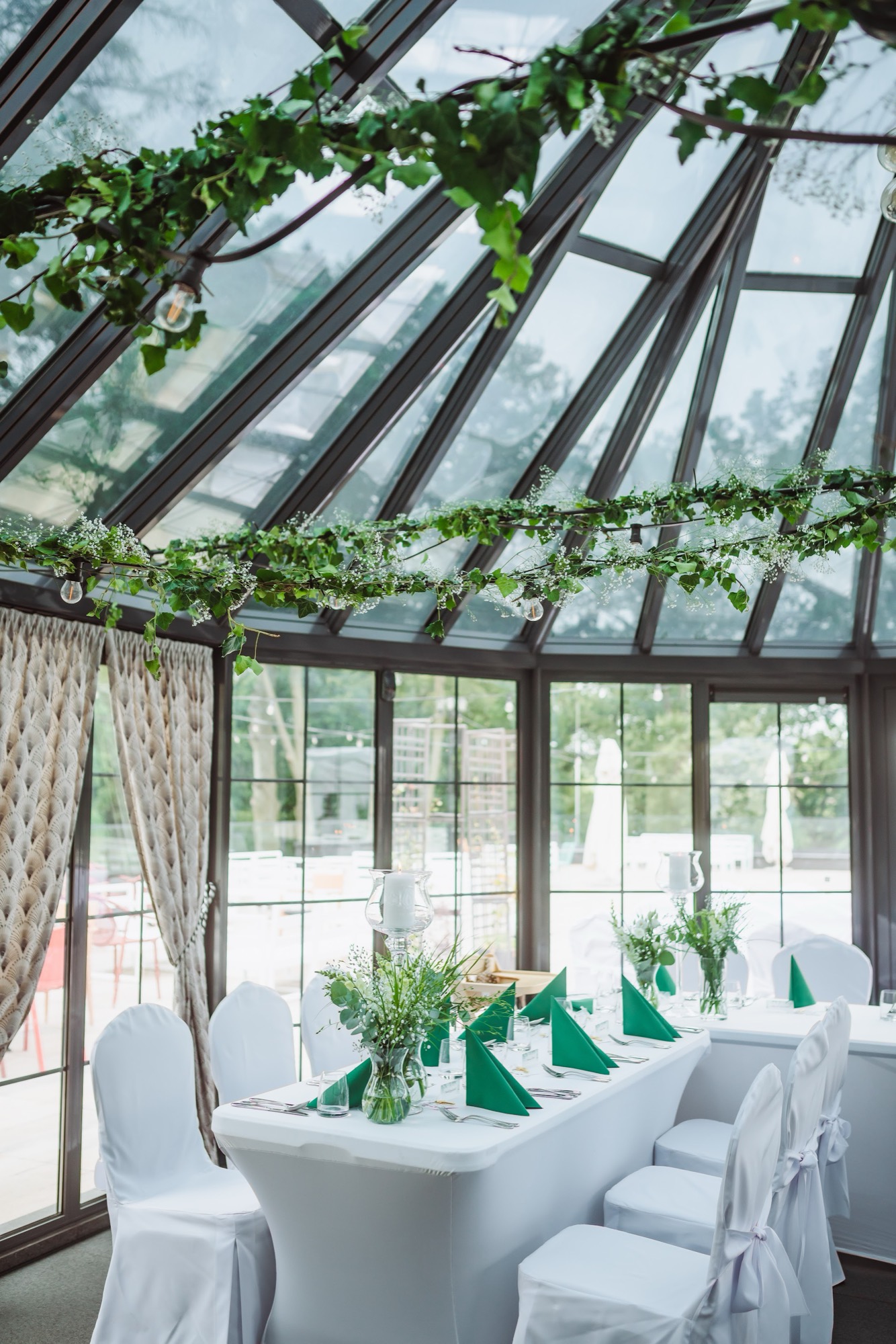 Sala w oranżerii z zielonymi girlandami pod szklanym dachem